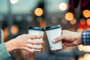 Close up on two people clinking single-use coffee cups, which have traditionally been difficult for paper recycling companies to process.