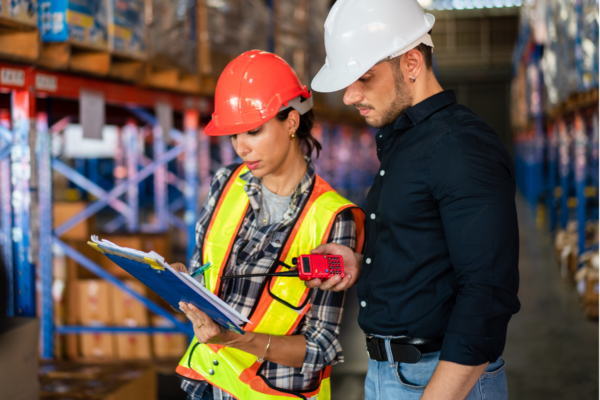 Facility managers in hard hats reviewing documents in a warehouse during recycling budget planning.