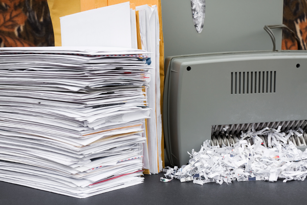stack of office paperwork beside a small desk shredder illustrating why you should choose professional document shredding services for businesses for large file cleanouts